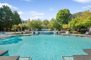 Lawrenceville apartment for rent - Lawrenceville, GA, Apartments with In-Unit Washer and Dryer - Parc at 980 - Resort Style Swimming Pool With Sparkling Water, Tiered Water Feature, Lounge Seating, And Lush Greenery Under Blue Sky.