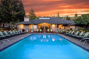 Hillsboro apartment for rent - Hillsboro, OR pet Friendly Apartments - Club at Tanasbourne - Resort Style Outdoor Pool With Lounge Chairs, Clubhouse Patio, And Sunset Sky Over Landscaped Community Grounds