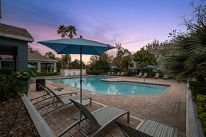 Jacksonville apartment for rent - Westside Jacksonville, FL, Apartments Near Oakleaf Town Center - Westland Park - A Swimming Pool Area Features Lounge Chairs, Blue Umbrellas, And Palm Trees.