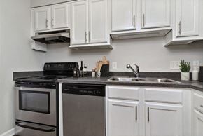 Raleigh apartment for rent - Pet-Friendly Apartments in Raleigh, NC - Bridges at North Hills - A Kitchen With White Cabinets, Dark Countertops, A Double Sink, A Stainless Steel Stove, And A Dishwasher.