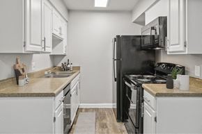 Tucson apartment for rent - Pet-Friendly Affordable Apartments in East Tucson, AZ - Hampton Park - A Kitchen With White Cabinets, Tan Countertops, Double Sink, Black Refrigerator, Electric Stove, And Microwave.