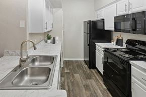 Garland apartment for rent - Dog-Friendly Apartments in Garland, TX - The Belmont at Duck Creek - A Kitchen With White Cabinets, Marble Look Countertops, Double Stainless Steel Sink, And Microwave.