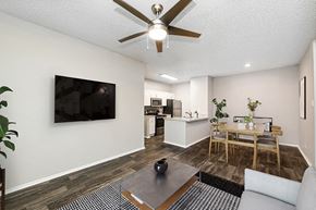 Dallas apartment for rent - Dog-Friendly Luxury apartments in North Dallas, TX - Dallas North Park - Living Room With Ceiling Fan, Wall-Mounted Television, Coffee Table, and Kitchen Breakfast Bar.