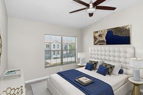 North Las Vegas apartment for rent - Apartments in North Las Vegas, NV, with In-Unit Washer and Dryer - Azure Apartment Homes - Bright Bedroom With Tufted Headboard, Ceiling Fan, Blue Bedding, And Large Window With Blinds.