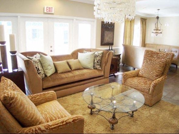 Pensacola apartment for rent - A living room with a tan couch, a glass coffee table, and a chandelier at Arbours at Ensley Apartments, Pensacola, 32514