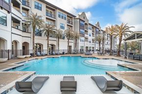 Baton Rouge apartment for rent - A swimming pool surrounded by lounge chairs and palm trees in front of a multi-story apartment building at The Addison, Baton Rouge, LA