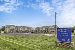 Shippensburg apartment for rent - A sign for Normandy Lofts is in front of a building with a grassy area in the foreground.