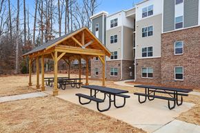 Dallas apartment for rent - A wooden pavilion with picnic tables is situated in front of a brick building.