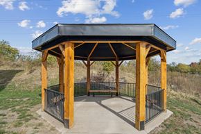 Johnston apartment for rent - A wooden pavilion with a black roof and metal railings is situated in a grassy area.