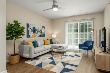 Wheeling apartment for rent - A living room with a grey couch, a blue chair, a plant, and a painting on the wall.