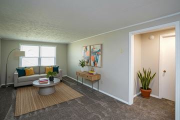 Shinnston apartment for rent - A living room with a grey couch, a coffee table, a potted plant, and a painting on the wall.