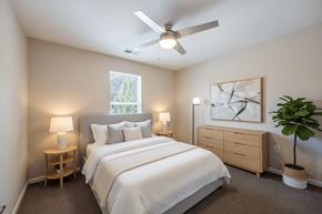 Zebulon apartment for rent - A bedroom with a large bed, a ceiling fan, and a window with a view of trees.