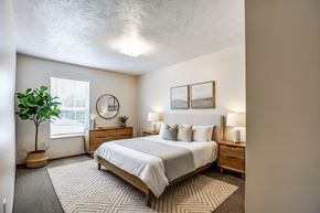 Weirton apartment for rent - A bedroom with a large bed, nightstands, and a potted plant.