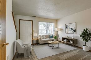 Ottawa apartment for rent - A living room with a grey sofa, a grey armchair, a wooden coffee table, a white side table, a white lamp, a white door, a white wall, a brown rug, a brown floor, a brown table, a