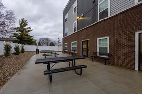 Columbus apartment for rent - A series of black picnic tables are lined up on a concrete patio outside of a brick building.