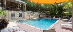 Austin apartment for rent - A pool with a stone wall and a patio with chairs and umbrellas.