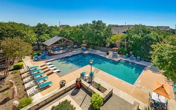 Austin apartment for rent - A large outdoor swimming pool surrounded by lounge chairs and trees.