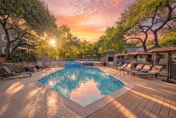 Austin apartment for rent - A sunset view of a pool surrounded by trees and lounge chairs.