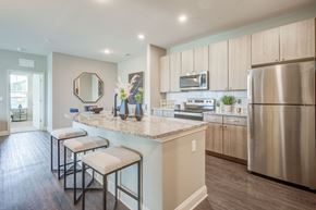 Kannapolis apartment for rent - one bedroom kitchen with gooseneck black faucet on the island,  woodgrain light cabinets, stainless steel appliances, granite countertops, kitchen table with blue leather chairs, 6-panel white doors, woodlike plank flooring, and laundry room off the kitchen