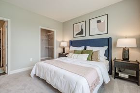 Kannapolis apartment for rent - bedroom with plush carpet, white trim and taupe walls, bed with blue velvet headboard and two lamps on either side nightstand, walk-in closet and entry to the bathroom