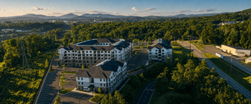 Gallatin apartment for rent - A large white building with a black roof is surrounded by trees and has a parking lot in front.