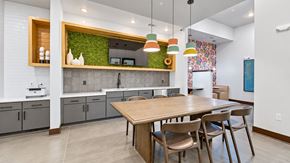Lawrenceville apartment for rent - Clubhouse kitchen with a communal table, colorful pendant lights and a green accent wall at Argento at Sugarloaf.