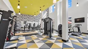 Lawrenceville apartment for rent - Fitness center with strength machines, free weights and treadmills beneath a yellow ceiling at Argento at Sugarloaf.