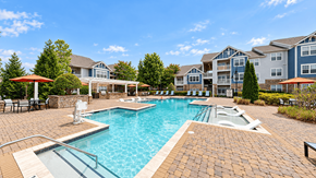 Indian Land apartment for rent - Outdoor swimming pool surrounded by a paved deck, lounge chairs, and umbrellas at Enclave at Bailes Ridge in Indian Land, SC.