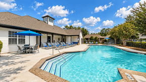 Cartersville apartment for rent - View across the Icon Cartersville swimming pool toward lounge chairs, umbrellas, and the clubhouse.