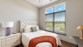 Carmel apartment for rent - Apartment bedroom with a tufted headboard, bedside dresser and large window at VER at Proscenium in Carmel, IN.