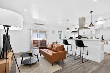 Los Angeles apartment for rent - A modern living room with a brown leather sofa and a white kitchen in the background.