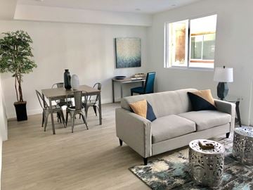 Reseda apartment for rent - A living room with a grey couch, a dining table with chairs, a desk with a chair, a floor lamp, and a rug.