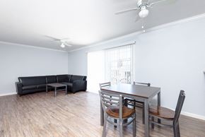 Long Beach apartment for rent - A living room with a black couch, a wooden dining table, and a ceiling fan.