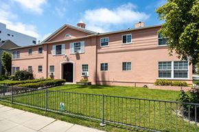 Beverly Hills apartment for rent - a pink building with a green lawn and a metal fence in front of it