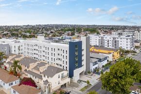 Los Angeles apartment for rent - A modern building with a blue accent wall is surrounded by other buildings and houses.