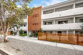 Los Angeles apartment for rent - A modern building with a white and brown facade is surrounded by a gravel area and a wooden fence.