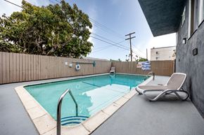 Los Angeles apartment for rent - a swimming pool with a chaise lounge chair and a privacy fence with trees in the background