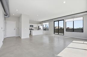 Chicago apartment for rent - A spacious, empty room with a kitchen area and a view of the city through the windows.