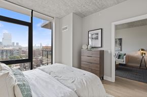 Chicago apartment for rent - a bedroom with a bed and a view of Chicago and floor to ceiling windows and wide plank flooring and tall ceilings