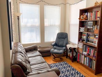 Chicago apartment for rent - A living room with a brown leather couch, a blue chair, and a bookshelf filled with books.