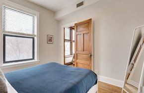 Chicago apartment for rent - A bedroom with a bed, a window, a door, and a mirror.