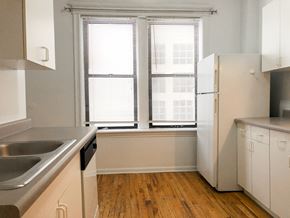 Chicago apartment for rent - A kitchen with a white refrigerator, wooden floors, and a window with blinds.