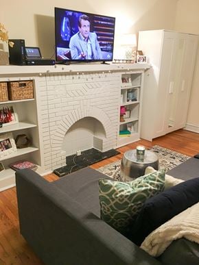 Chicago apartment for rent - A grey couch with a green pillow is in front of a white fireplace.