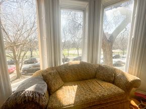 Chicago apartment for rent - A couch with a blanket on it is in front of a window with a view of a parking lot and trees.