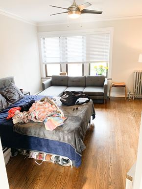 Chicago apartment for rent - A messy bedroom with a bed covered in clothes and a couch in the background.