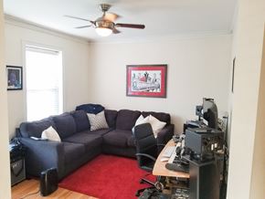 Chicago apartment for rent - A living room with a grey couch, a red rug, and a ceiling fan.