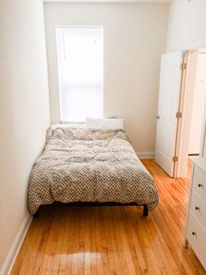 Chicago apartment for rent - A bed with a white and black patterned cover sits in a room with wooden floors and white walls.