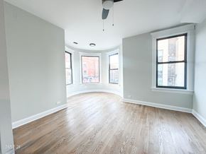 Chicago apartment for rent - A spacious room with wooden floors and a ceiling fan.