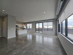 Chicago apartment for rent - A large, empty room with a concrete floor and a kitchen area in the background.
