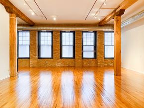 Chicago apartment for rent - A large empty room with wooden floors and brick walls.